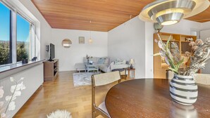 A modern living room with a wooden ceiling, a round dining table, and a view of the outdoors.