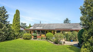 A traditional house with a tiled roof, surrounded by well-maintained lawns and various shrubs.