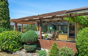 Ein überdachter Patio-Bereich mit einer Holz-Pergola, einem Tisch mit Stühlen und Blick auf den Garten durch große Fenster.