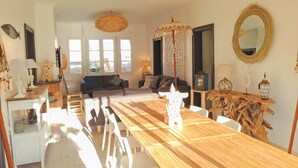 Un salon spacieux avec une table à manger en bois, des chaises blanches, un canapé et un grand miroir.