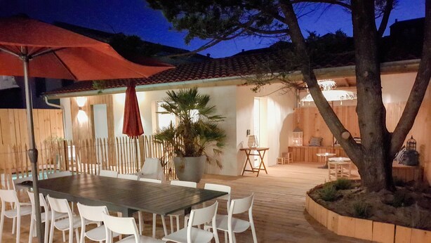 Une terrasse extérieure avec une table et des chaises, un parasol rouge et une clôture en bois.