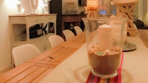 Un coin repas avec une table en bois, des chaises blanches et un vase en verre contenant des bougies.