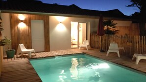 Une piscine dotée d’une terrasse en bois, entourée de chaises longues blanches et d’une clôture en bois.