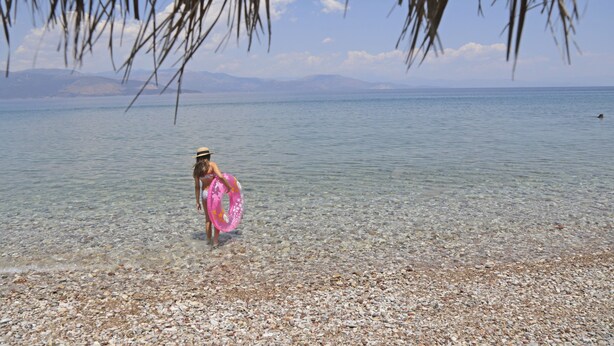 A pebbled beach with clear water and distant mountains.