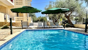 A rectangular swimming pool with clear blue water, surrounded by lounge chairs and green umbrellas.