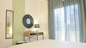 A hotel room with a bed, a desk with a lamp, a mirror, and a window with curtains.