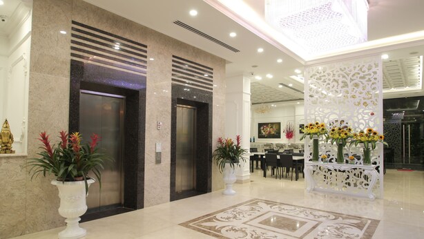 A modern lobby with two elevators, a reception desk, and decorative plants. - Acnos Grand Hotel (Ho Chi Minh City)