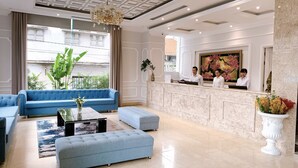 Un hall d’hôtel moderne avec un canapé bleu, un comptoir d’accueil en marbre et une grande fenêtre donnant sur la rue.