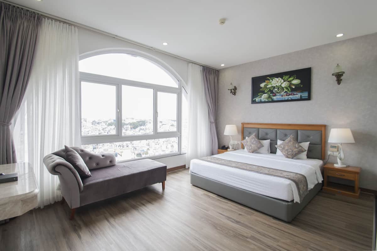 Un dormitorio moderno con una cama grande, un sofá, una mesita de noche y una ventana con cortinas.