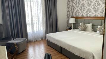 A hotel room with a large bed, a chair, a desk, and a window with curtains.