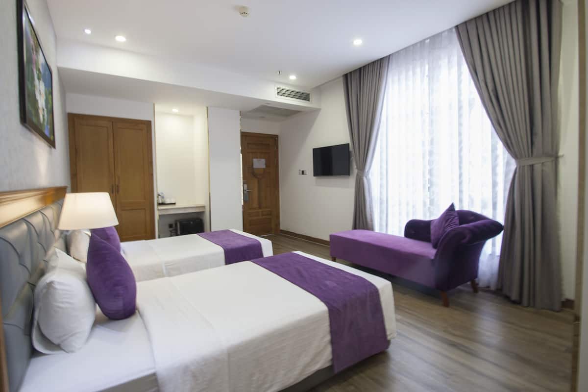 Habitación de hotel con dos camas, un sofá, un televisor y un ventanal grande con cortinas.