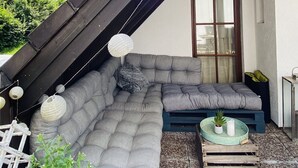 A modern outdoor seating area with a large grey sectional sofa, a small table with a potted plant, and decorative paper lanterns. - Holiday rental Kallenbachtal I (Löhnberg)