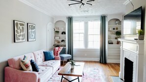 A living room with a pink sofa, a blue armchair, a wooden coffee table, and a fireplace. - Charming 2BR Getaway | Pets Welcome in Cloverdale (Montgomery)