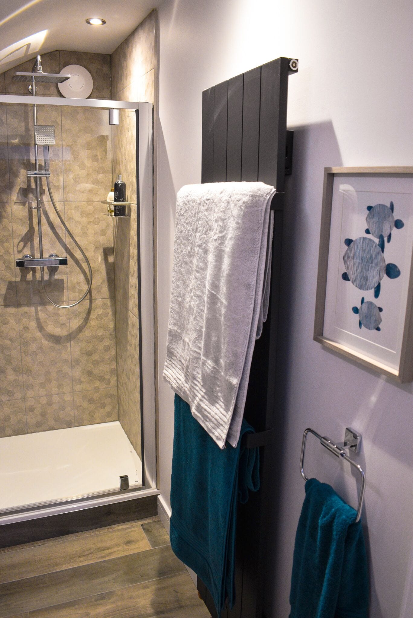 Un baño moderno con ducha envuelta en cristal, una bañera blanca y un perchero con varias toallas.