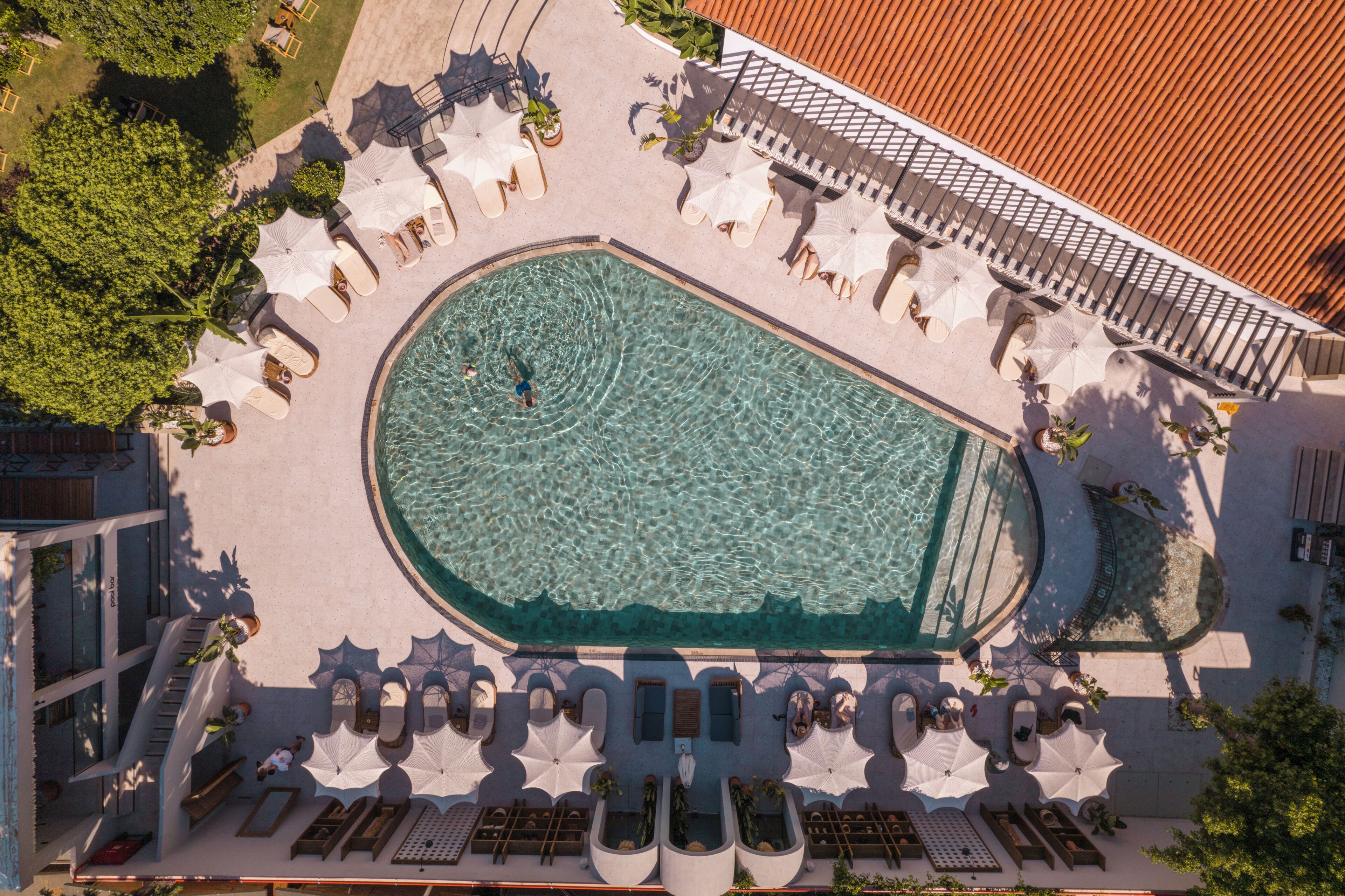 An aerial view of a hotel pool area with sun loungers, umbrellas, and a clear swimming pool.