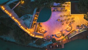 Eine Luftaufnahme eines Anwesens am Wasser mit einer gewölbten Terrasse, Sitzbereichen im Freien und einem Pool.
