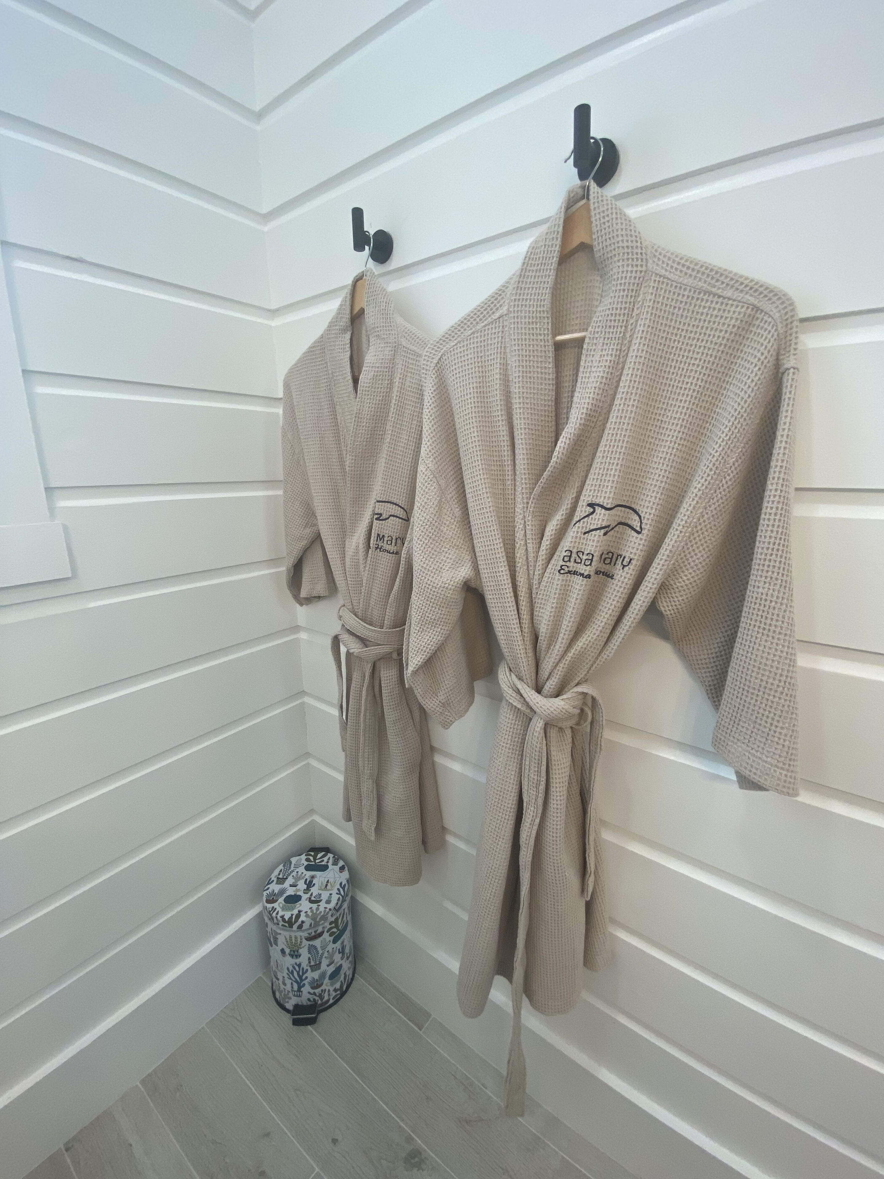 Two beige robes hanging on hooks in a room with white paneled walls and a wooden floor.