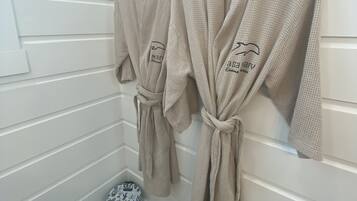Two beige robes hanging on hooks in a room with white paneled walls and a wooden floor.