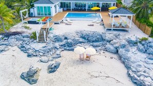A beachfront property with a swimming pool, lounge chairs, and umbrellas. - Casa Mary : The Ultimate Luxury Beachfront Home in the Exumas (Jimmy Hill)
