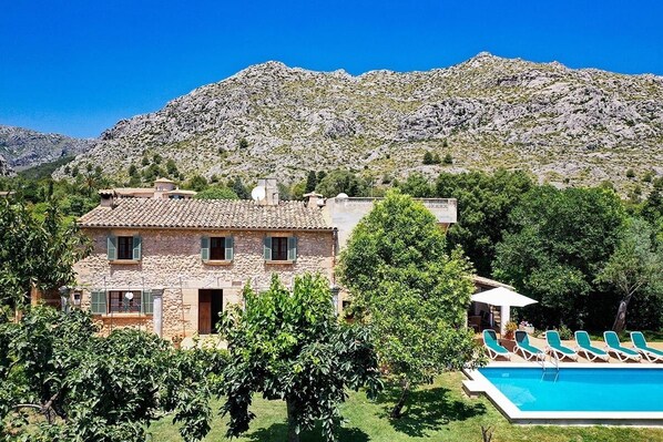 A stone house with a swimming pool and lounge chairs, surrounded by trees and mountains. - Finca Puna with pool, quiet location, A/C, Wifi, 7 km to the beach (IB)