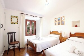 A room with two beds, a chair, a window with curtains, and a wall with framed pictures. - Finca Puna with pool, quiet location, A/C, Wifi, 7 km to the beach (IB)