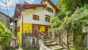 Ein zweistöckiges Gebäude mit einer gelb-weißen Fassade, Holzläden und einer Steintreppe, die zum Eingang führt.
