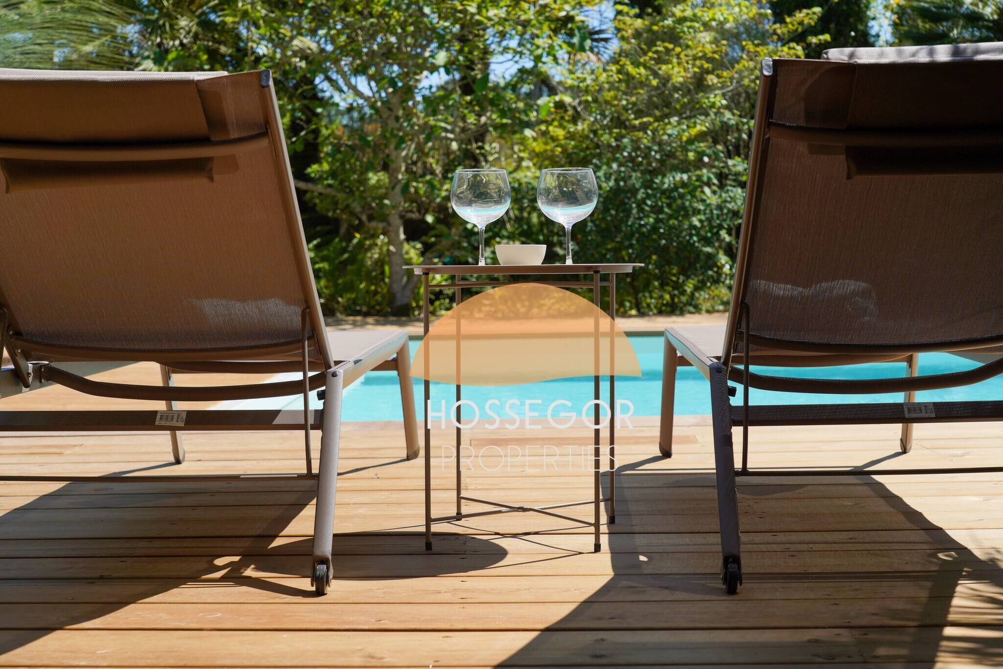 Two lounge chairs facing a pool with a table and two glasses between them.