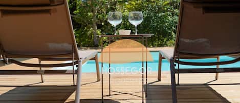 Two lounge chairs facing a pool with a table and two glasses between them.