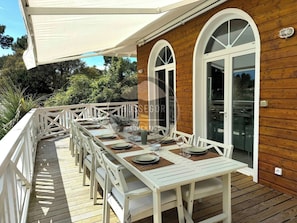 A covered outdoor dining area with a long table set for multiple people, white chairs, and a wooden deck. - Case du Golf - Seignosse - Pool - Golf - Beach (Seignosse)