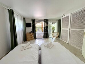 A hotel room with two beds, a TV, a wooden dresser, and a view of the outside. - Case du Golf - Seignosse - Pool - Golf - Beach (Seignosse)