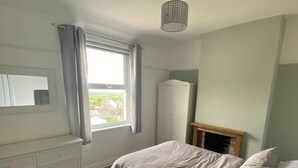 Un dormitorio con cama, cómoda, armario, ventana con cortinas y lámpara colgante.