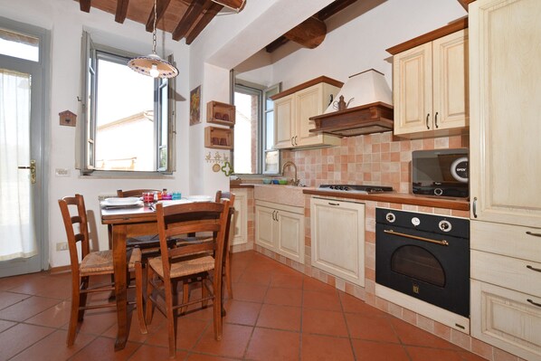 A kitchen with wooden cabinets, a dining table with chairs, a window, and an oven. - Casa Guna (Asciano)