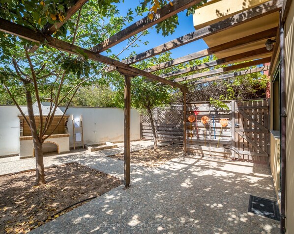 Un espacio al aire libre techado con una pérgola, un muro de ladrillo y una valla de madera.