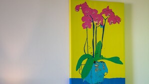 A room with a wall-mounted painting of pink orchids, a lamp, and a bookshelf. - Fluo Seaside Apartment (Aegina)