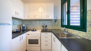 A compact kitchen with white cabinets, a built-in oven, a microwave, and a sink. - Fluo Seaside Apartment (Aegina)