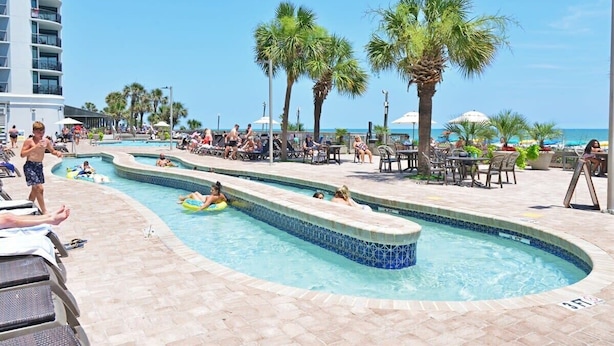 A pool area with multiple swimming pools, palm trees, and outdoor seating.