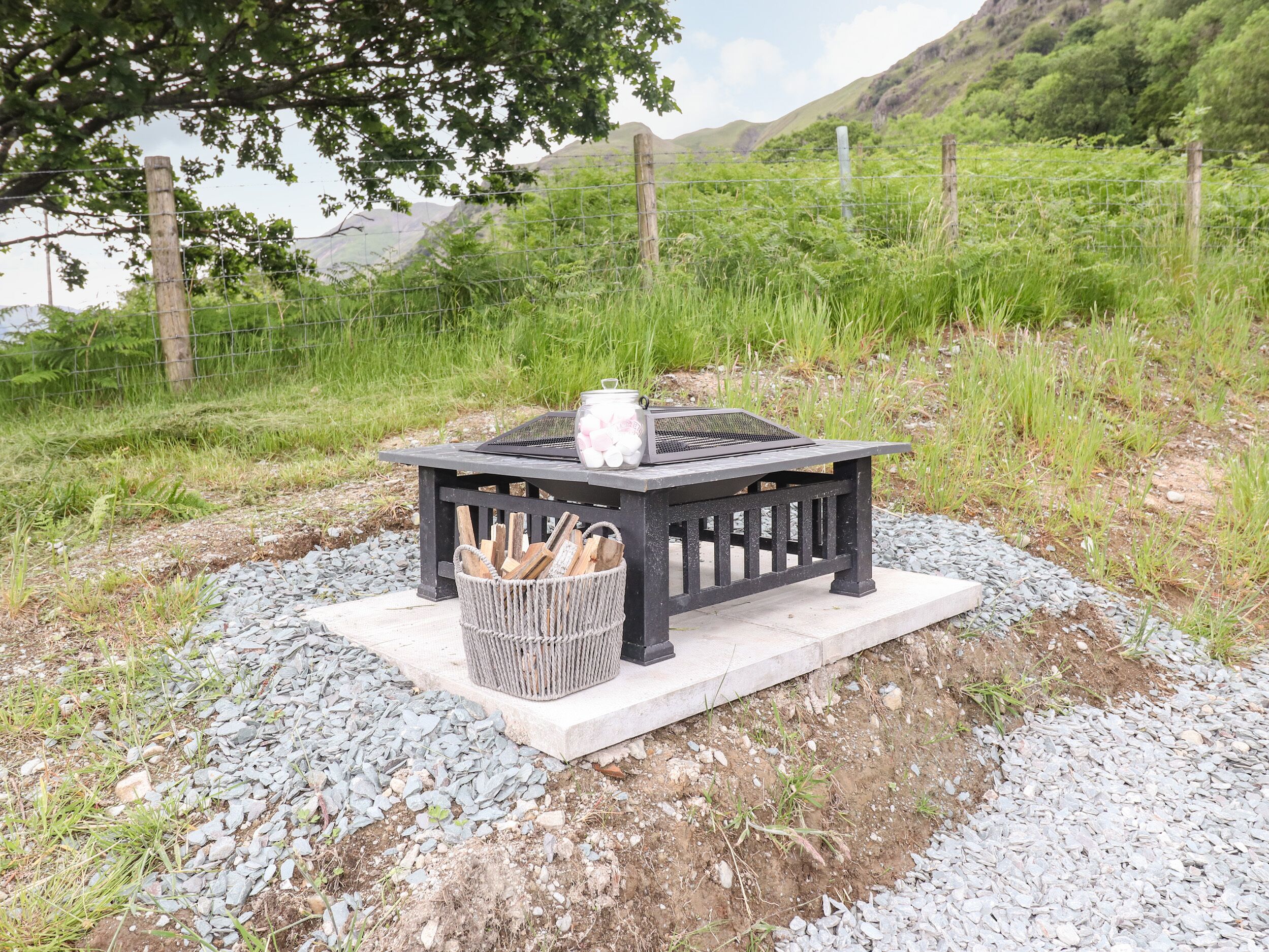 A picnic setup with a table, a basket of wood, and a pot of marshmallows.