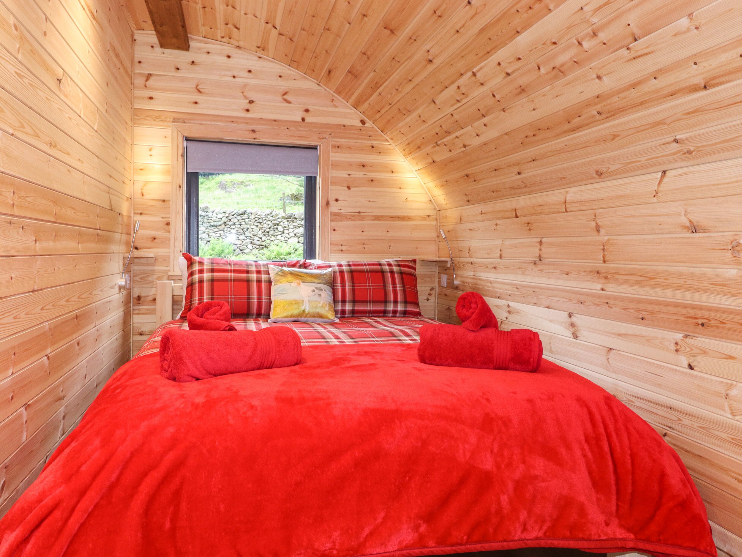 A cozy wooden cabin room with a bed, pillows, and a window.