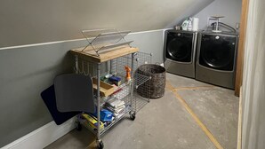 Een wasserette met twee wasmachines, een metalen kar met schoonmaakmiddelen en een betonnen vloer met gele lijnen.
