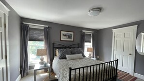 Een slaapkamer met een bed, twee nachtkastjes, een raam met gordijnen, een deur en een plafondlamp.