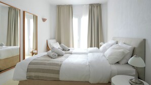 A hotel room with two beds, a large mirror, a bedside table with a lamp, and a view of the outdoors through the window. - Villa Super Two (Mykonos)