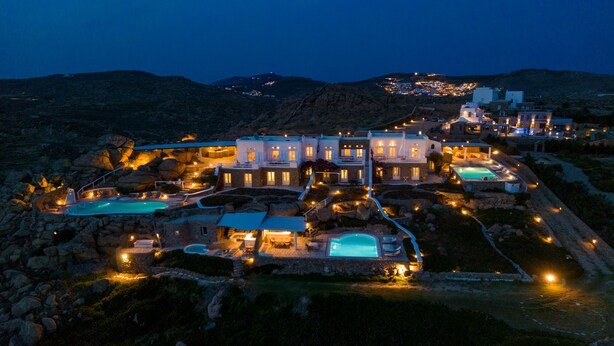 A luxurious resort with multiple swimming pools, a well-lit main building, and a scenic mountainous backdrop. - Villa Super Two (Mykonos)