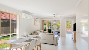 A modern living room with a dining area, a sofa, a TV, and a view of a swimming pool.