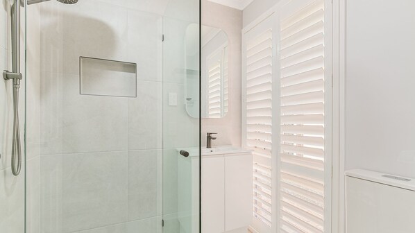 A modern bathroom with a glass shower enclosure, a white sink, and a mirror.