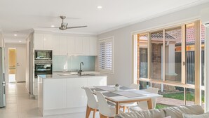Une cuisine moderne avec des meubles blancs, un four encastré et un coin repas comprenant une table et des chaises.