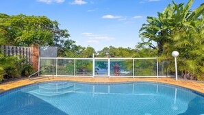 Une piscine dotée d’une enceinte en verre, entourée d’une végétation luxuriante et surplomb ée par un ciel bleu azur.