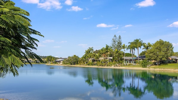 A serene lakeside view with a clear sky, surrounded by lush greenery and residential buildings.
