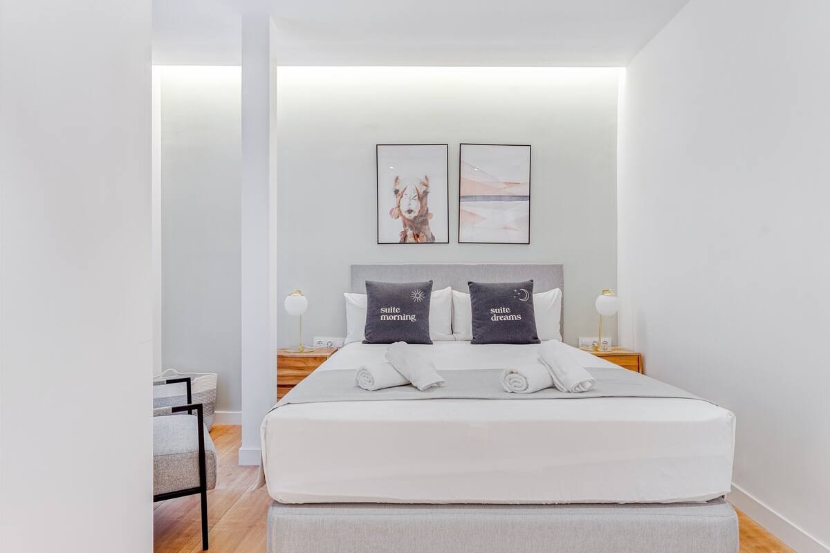 Una habitación de hotel moderna con una cama grande, dos mesitas de noche con lámparas y una obra de arte en la pared.