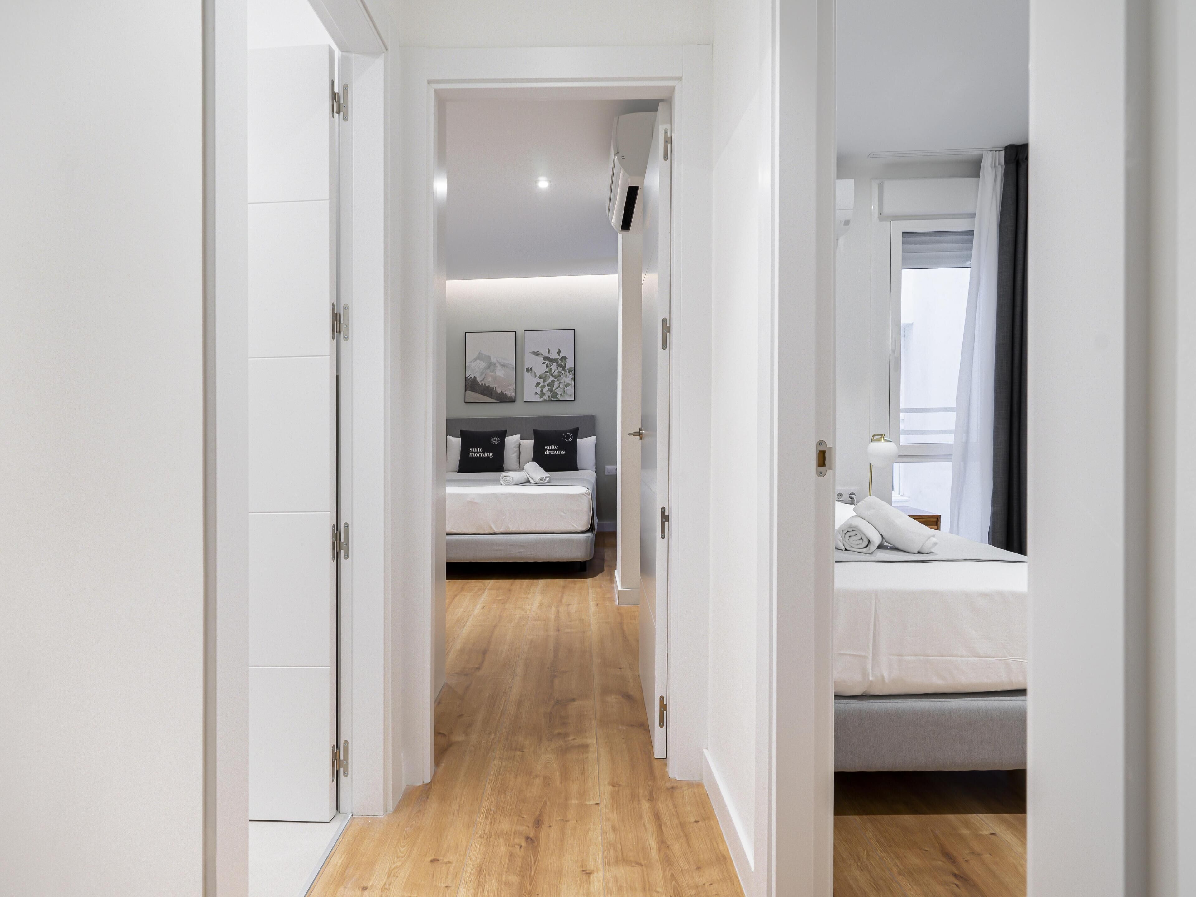Una habitación de hotel moderna con piso de madera, cama con ropa blanca, mesita de noche y ventana con cortinas.