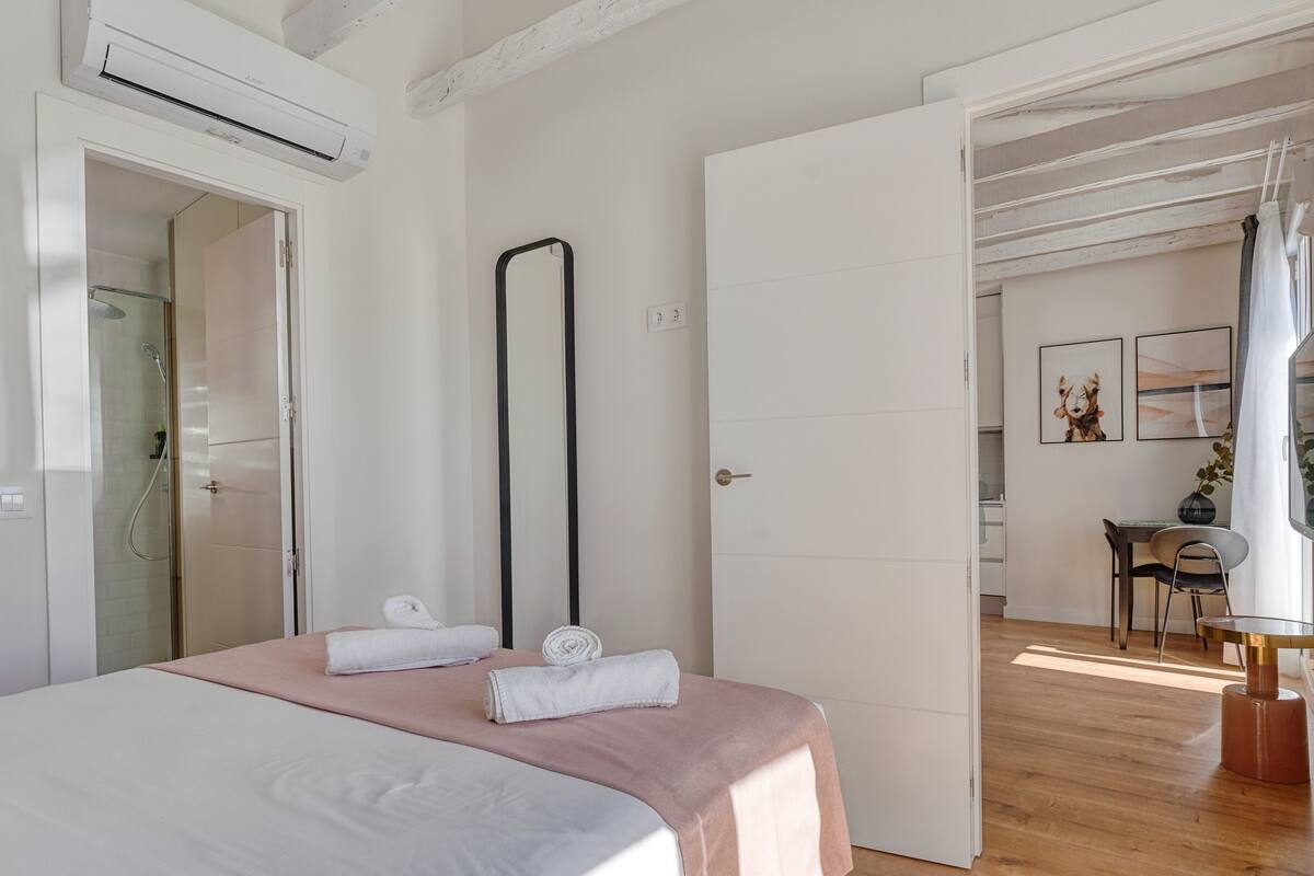 Un dormitorio con cama, ducha, puerta que da a un comedor y espejo.